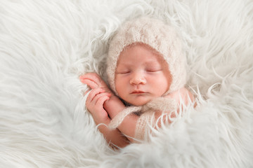 Новорожденный ребенок в вязанном чепчике спит на...