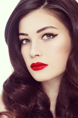 Vintage style close-up portrait of young beautiful woman with winged eyes make-up, red lips and long curly hair