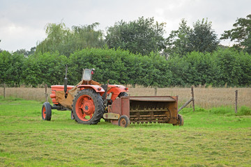 Old abandoned tractor with rusty hay turner in meadow