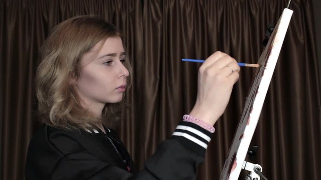 Girl Learns to Draw. Girl draws a picture at the easel with paint and brush. The girl is an aspiring artist
