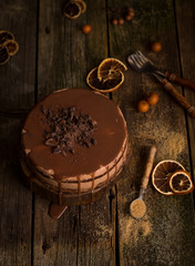 Homemade tasty chocolate naked cake with chip and liquid cream. It is on the old textured wooden rustic table, there is dried oranges, wooden spoon  with brown sugar 