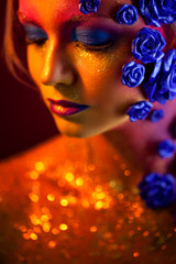 Portrait of young and attractive woman with art makeup. Fiery colors, glitter on face and floral decoration