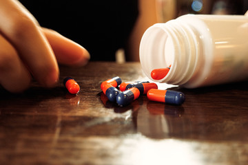 Orange-blue pills spilled out of bottle on polished wooden table and girls hand holding one of it