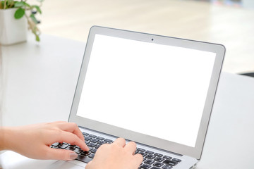 Woman's hands typing on a keyboard with blank screen laptop.