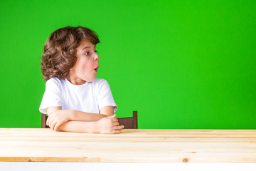 Curly resentful boy sitting half-turned mouth open, looking away. Close-up. Green background.