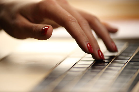 Main d'une jeune femme sur clavier d'ordinateur, informatique au féminin avec vernis rouge sexy
