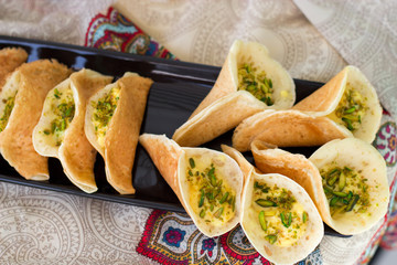 Traditional Arabic qataif crepes stuffed with cream and pistachios, prepared for iftar in Ramadan on paisley background above