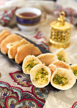 Traditional Arabic qataif crepes stuffed with cream and pistachios, prepared for iftar in Ramadan on paisley background above