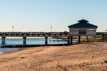 Morning light on fishing pier with sandy beach at Buckroe Beach in Hampton, Virginia.   - obrazy, fototapety, plakaty