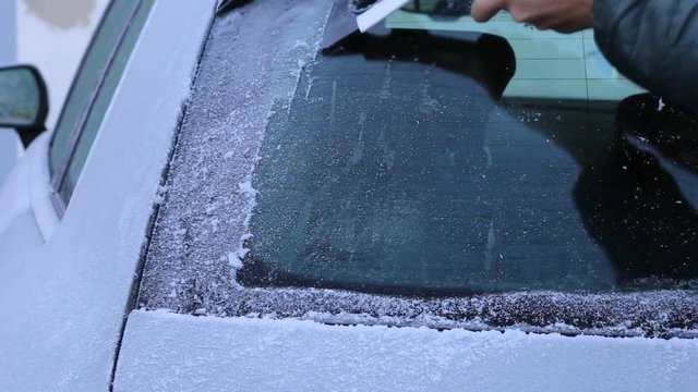 Mann kratzt Eis von der Heckscheibe seines Autos im Winter