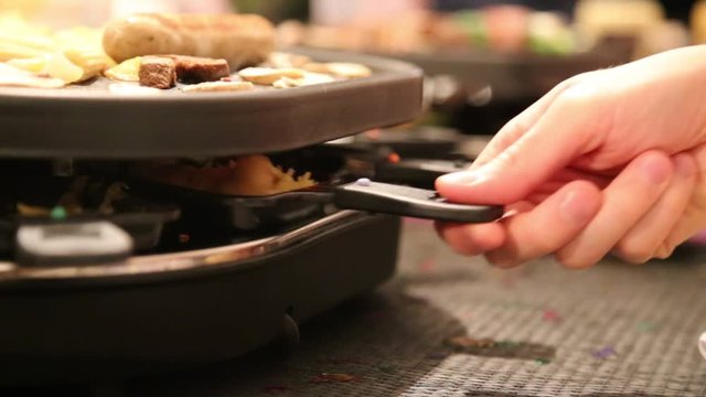 Mann nimmt Pf&auml;nnchen aus dem Raclette-Ofen an Silvester