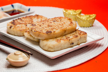 Turnip cake with sauce and white placemat on red background. People will eat turnip cake during Chinese New Year to pray for good fortune.It means be promoted step by step.The Chinese text is "spring"
