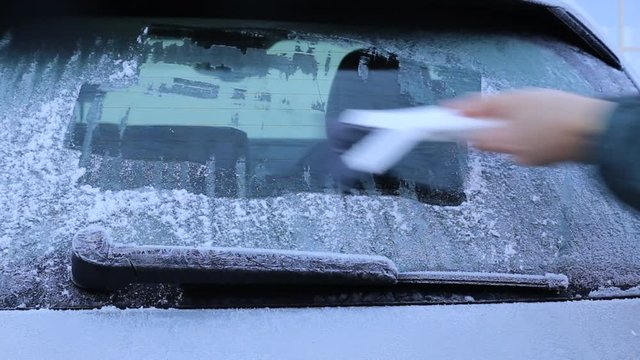 Mann kratzt Eis von der Heckscheibe seines Autos im Winter