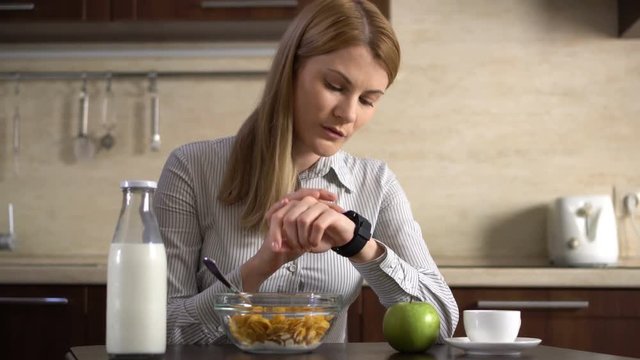 Beautiful attractive businesswoman having breakfast and sending a voice message via her smart watch.