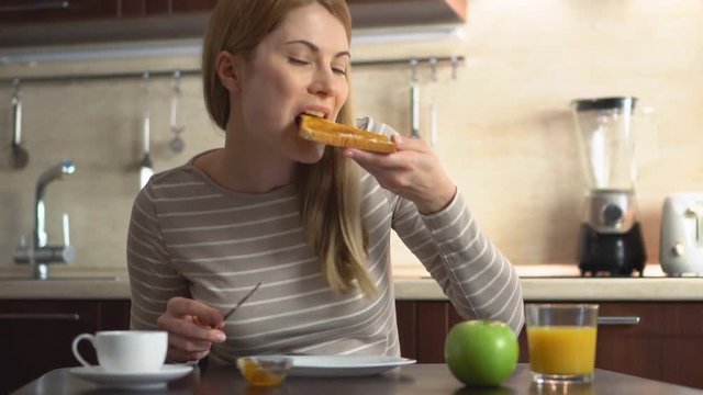 Beautiful young eating bread and butter with jam. Breakfast with coffee and juice in the kitchen.