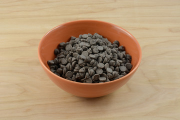 Chocolate chips in orange bowl on wooden table