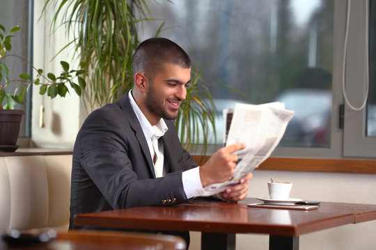 Smiling young businessman is reading newspaper while having a coffee break in a coffee shop