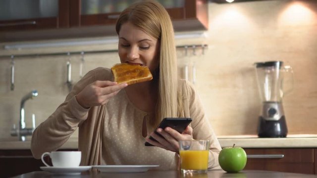 Beautiful young attractive woman eating her breakfast and browsing internet in the kitchen.