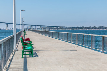 Pier with benches at Cesar Chavez Park in San Diego, California with Coronado Bridge. - obrazy, fototapety, plakaty