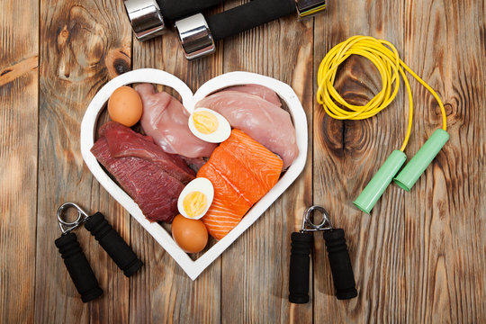 Proteins and dumbbells. Fish, cheese, eggs, meat, chicken  heart on wooden background