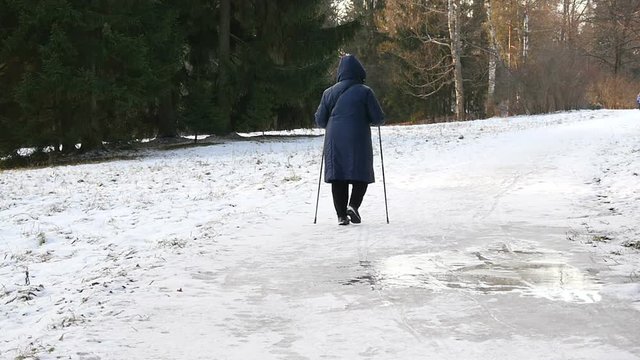 Elderly woman walks Nordic walking in the winter park