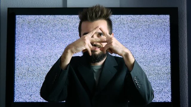 Bearded man in suit showing his eye in triangle as the Eye of Providence while moving forward and backwards with large grainy screen behind him.