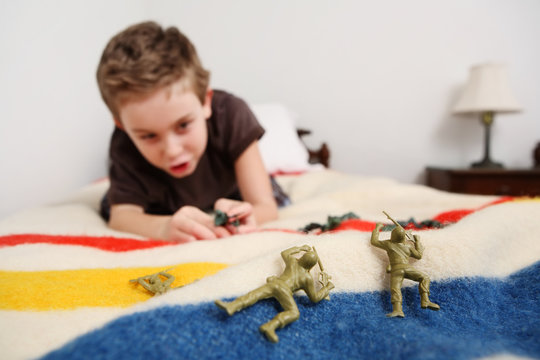 Young boy laying on his bed playing with toy soldiers