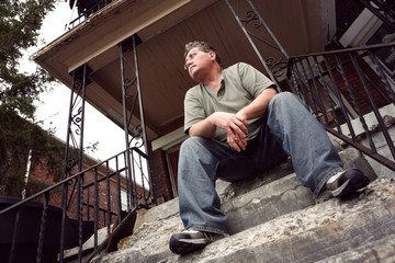 Middle aged man sitting on the steps of a house