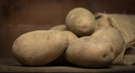 Potatoes from bag lying on wooden background