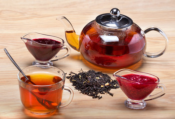 Пить полезный чай с вареньем.Заварной стеклянный чайник,чашка с чаем,два вида варенья.\Пить полезный чай с вареньем.Заварной стеклянный чайник,чашка с чаем,два вида варенья на деревянном столе.