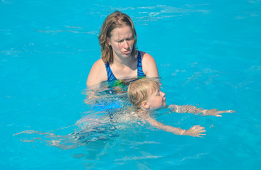 Eine junge Mutter gibt Ihrem Kind den ersten Schwimmunterricht im blauen Wasser