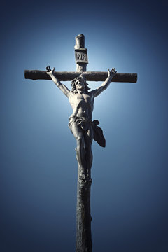 Statue of Jesus Christ on a cross. Blue sky in the background. Vertically. Edited as a vintage photo with dark edges.