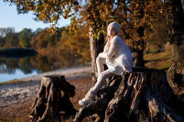A girl in white clothes and a hat sitting on a stump on the beach at sunset