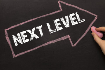 Next Level - female hand with chalk and arrow on blackboard