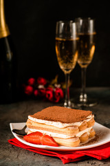 Tiramisu with strawberry and glasses of champagne on the table. Valentines concept. Dark moody style.