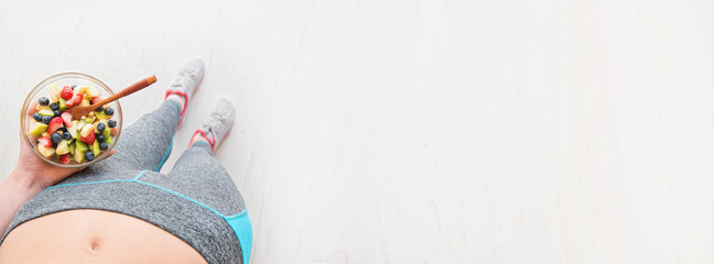 Young woman is eating a healthy fruit salad after a workout. Fitness and healthy lifestyle concept. 