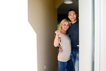 happy young couple at the front door of new house showing proudly home key