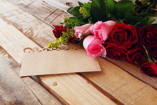bouquet of roses next to letter on wooden table