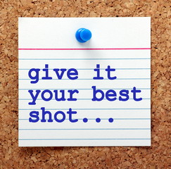 The words Give It Your Best Shot on a note card pinned to a cork notice board as a reminder to put in your best effort to achieve success