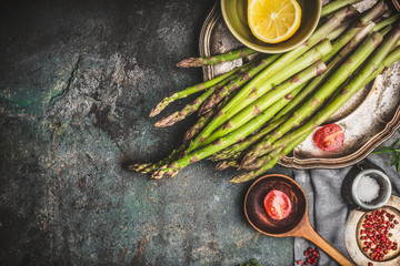 Green asparagus preparation with wooden cooking spoon and vegetables on rustic background, top view, border. Dark style - obrazy, fototapety, plakaty