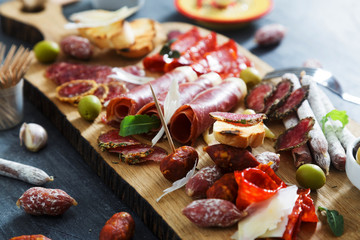 Cured meat platter of traditional Spanish tapas - chorizo, salsichon, jamon serrano, lomo - erved on wooden board with olives and bread