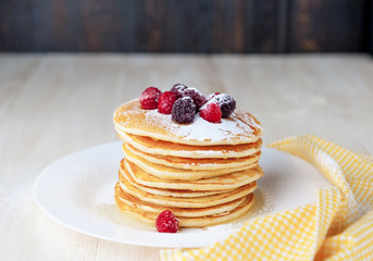 Pancake on a white plate with fruit and powdered sugar on a wooden background