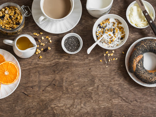 Breakfast setting over wooden table with copy space border. Yogurt, pumpkin granola, bagel, butter....