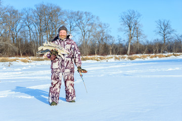 Bearded man is holding frozen fish after successful winter fishing at cold sunny day