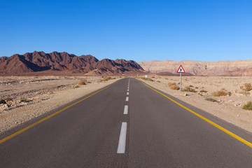 Fototapeta na wymiar Empty desert road with mountains and blue sky in the background
