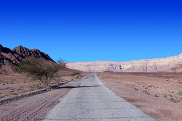 Empty desert road with mountains and blue sky in the background