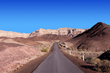 Empty desert road with mountains and blue sky in the background