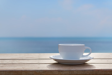 White coffe cup on wood table top with blurred sea sky backgroun