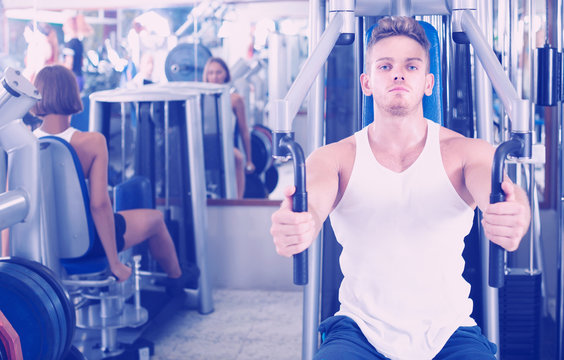 well trained man using pec deck gym machinery indoors