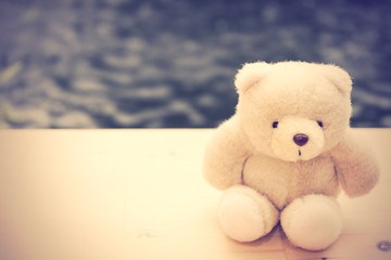 Cute teddy bear sit alone on wooden floor with pool background,r